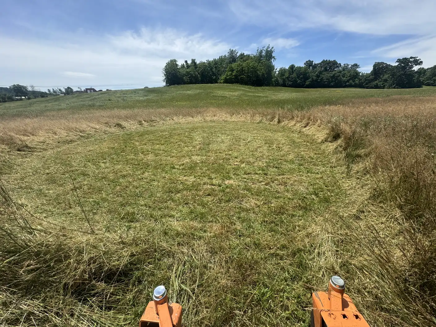 View from an orange zero-turn mower cutting a field.